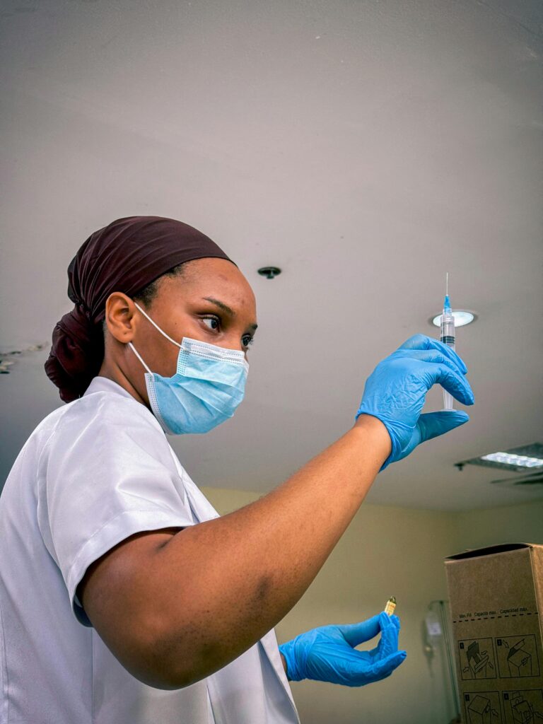 Medical professional wearing mask and gloves preparing injection in a healthcare setting.